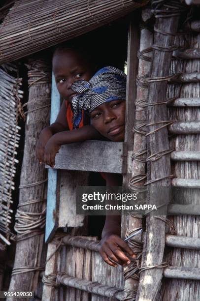 Femme à la fenêtre de sa maison avec son fils à Ganvié, Bénin.