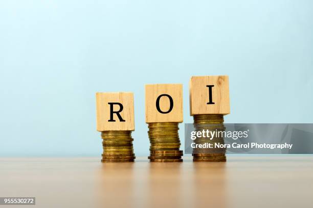 roi text written on wooden block with stacked coins - roi stock-fotos und bilder