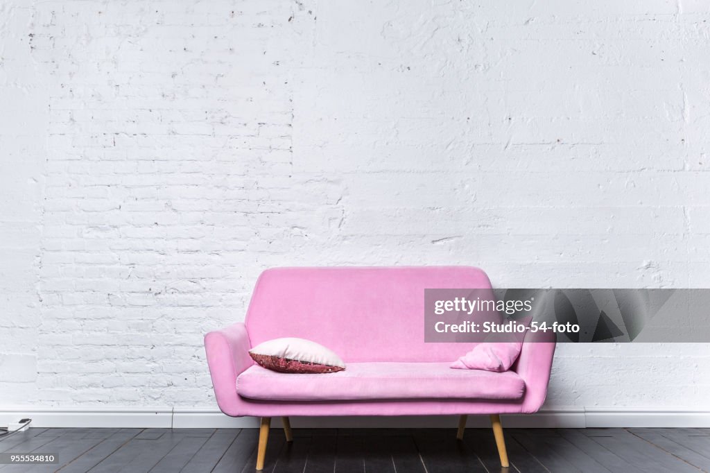 Sofá retro rosa contra la pared de ladrillo blanco