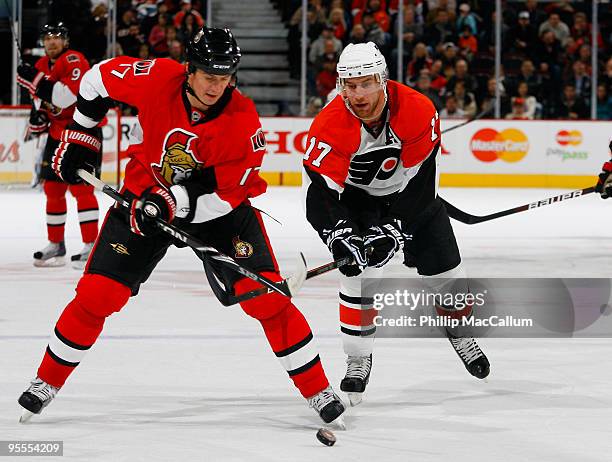 Filip Kuba of the Ottawa Senators tries to control a loose puck while fighting off the tight checking of Jeff Carter of the Philadelphia Flyers in a...