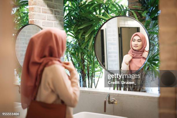 muslim woman with fixing hijab in restroom - vintage hand mirror stock pictures, royalty-free photos & images