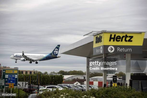 An Alaska Airlines Inc. Plane flies above the Hertz Global Holdings Inc. Rental location at LaGuardia Airport in the Queens borough of New York,...