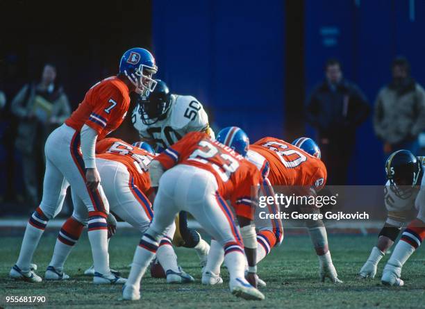 Quarterback John Elway of the Denver Broncos looks on from the line as scrimmage as he stands near running back Sammy Winder and offensive linemen...