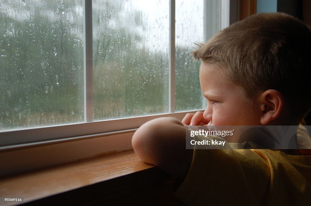 Young boy staring out a window as it rains