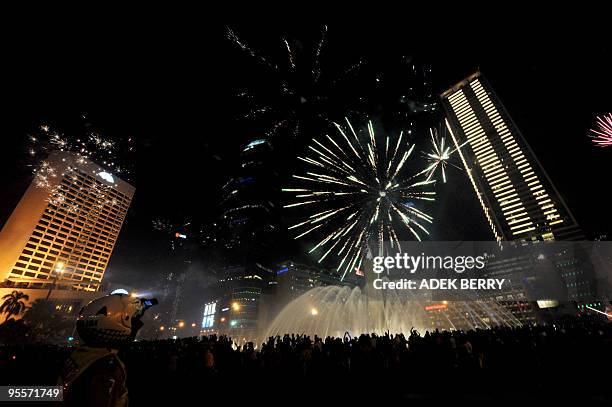 An Indonesian police takes a picture with his handphone as fireworks explode next to Jakarta landmark Welcome Statue during the New Year 2010...