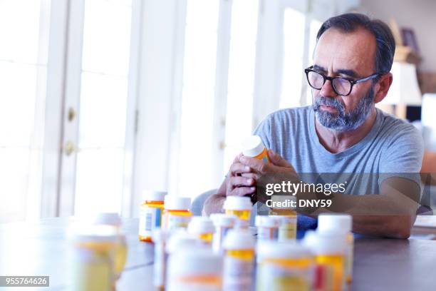 latino man sitting at table sorting through prescrption medications - medicine bottle stock pictures, royalty-free photos & images