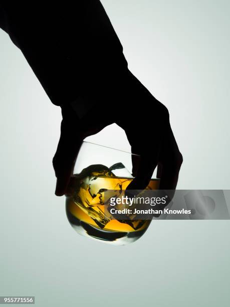 silhouetted male hand holding a glass of whiskey - alcoholic stock-fotos und bilder