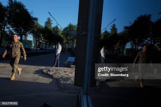 Pedestrian dressed in military uniform is reflected in the window of a store in Dushanbe, Tajikistan, on Saturday, April 21, 2018. Flung into...