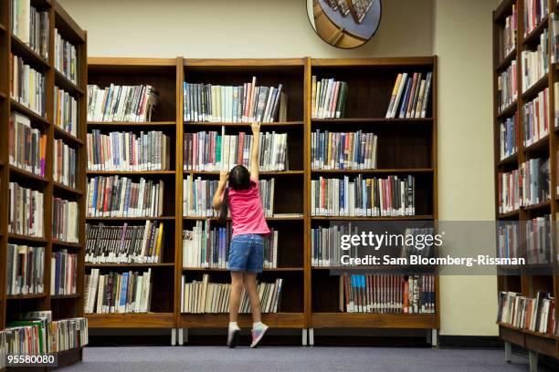 girl reading for book on library shelf - shelf strip stock pictures, royalty-free photos & images