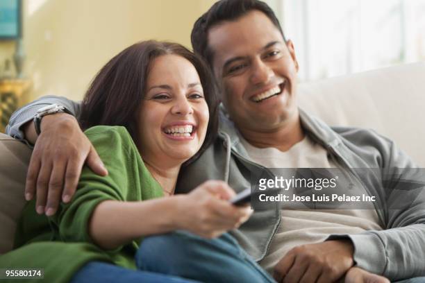 hispanic couple watching television - pareja de mediana edad fotografías e imágenes de stock