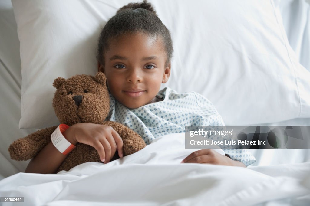 Mixed race girl in hospital bed with teddy bear