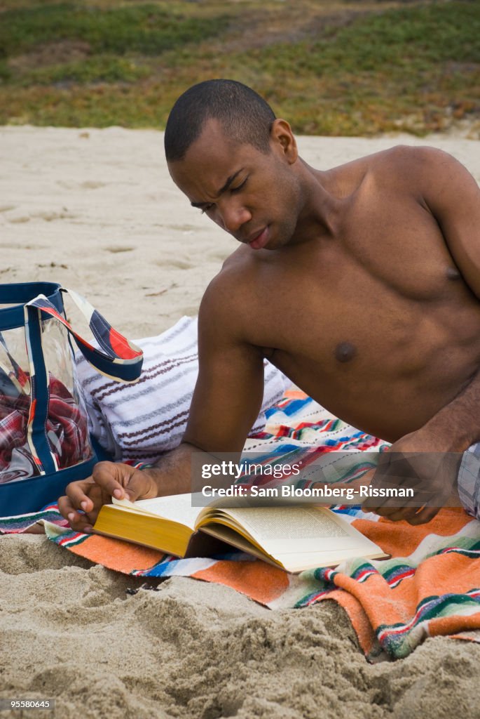 African man reading book on beach
