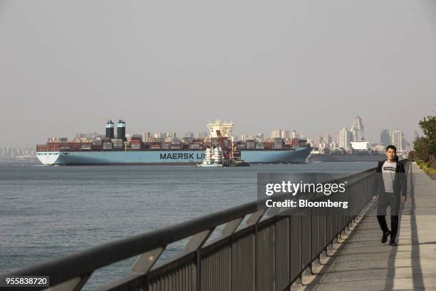 Man walks along the waterfront as the Marit Maersk cargo ship operated by A.P. Moller-Maersk A/S sets sail from the Qingdao Qianwan Container...