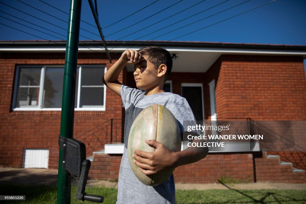 Portrait of Indigenous Australian aboriginal boy under hills hoist holding rugby ball