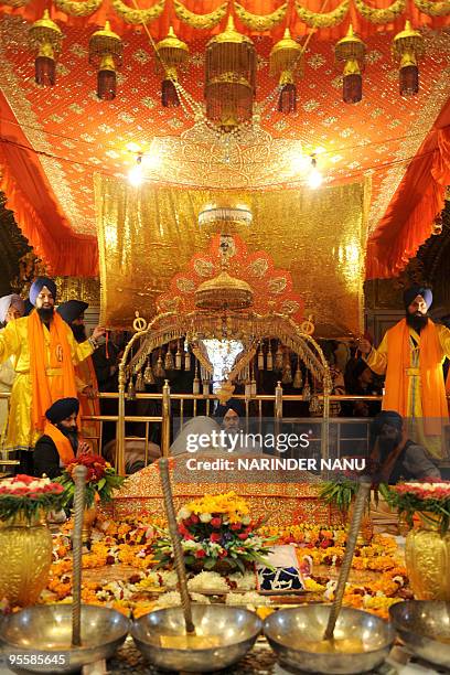 Indian Sikh priest Jagtar Singh sits behind the Sikh Holy Book - Guru Granth Sahib - as a 'Jalau', a splendour show of Sikhism's symbolic items, is...