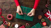 Woman tying gift box in the center of christmas decorating items on a wooden table