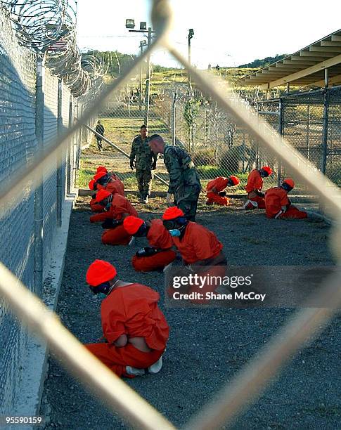 Detainees in orange jumpsuits sit in a holding area under the watchful eyes of Military Police at Camp X-Ray at Naval Base Guantanamo Bay, Cuba,...