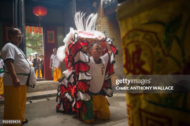 Member of a lion dance troupe lifts his mask as he kneels in front of an alter to celebrate the Tin Hau Festival at the Tai Shu Ha temple in the Yuen...