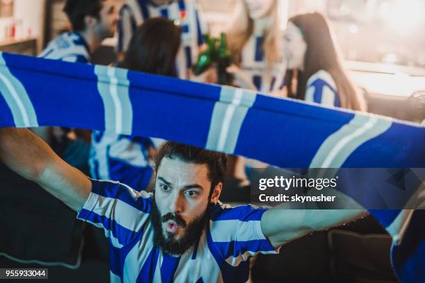 dedicated sports fan cheering for his team while watching a game on tv at home. - cachecol imagens e fotografias de stock