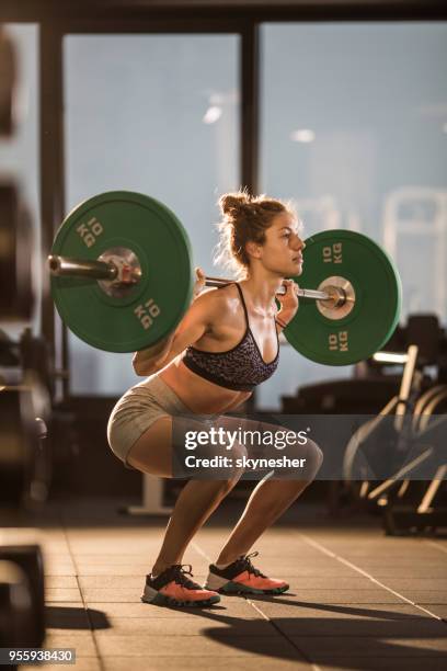 muscular build sportswoman exercising with barbell in a squat position. - barbell stock pictures, royalty-free photos & images