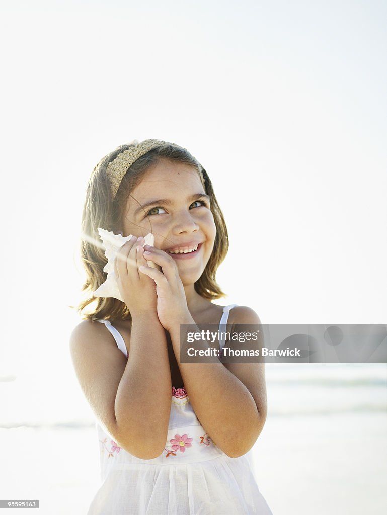 Young girl smiling holding seashell up to ear