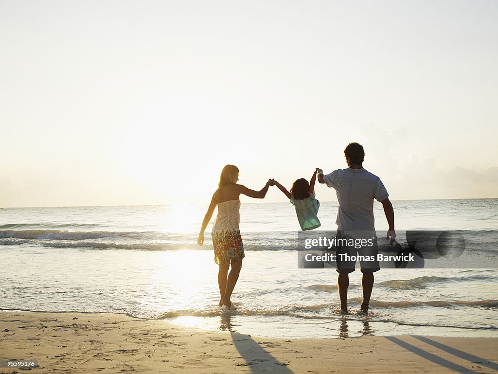 Mother and father swinging daughter by arms