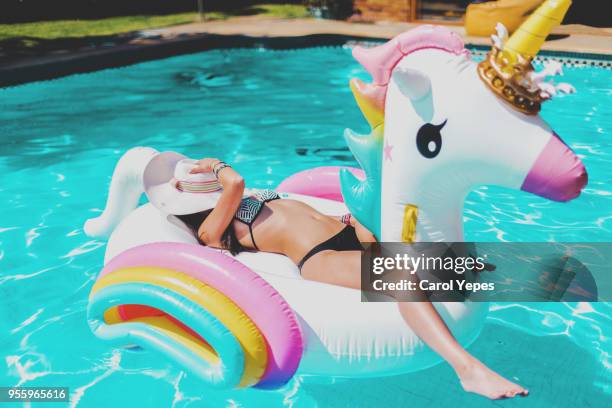 young woman lying in a big unicorn inflatable ring at pool in summer - inflate stockfoto's en -beelden