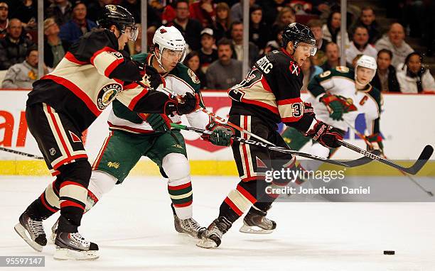 Duncan Keith and Kris Versteeg of the Chicago Blackhawks pursue the puck with Andrew Brunette of the Minnesota Wild at the United Center on January...