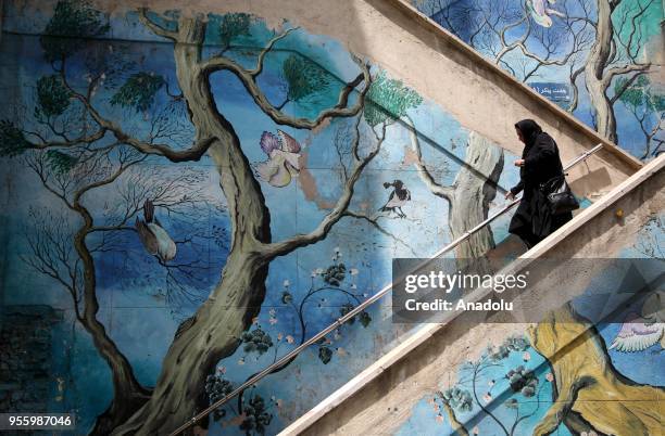 Woman walks down the stairs with mural paintings on the walls in Tehran, Iran on May 08, 2018.