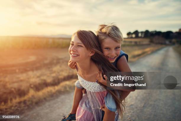 kleines mädchen geben ihrem bruder eine huckepack fahrt - bruder schwester stock-fotos und bilder