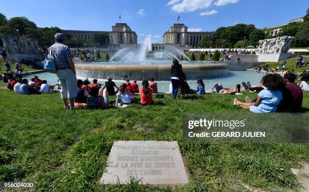 An instruction plate reads 'Lawn and bathing prohibited, risk of accidents, when water fountains are in use' as people enjoy the sun and warm spring...