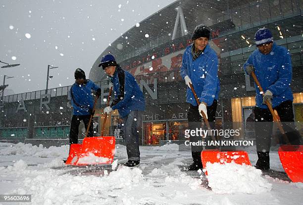Arsenal ground staff attempt to clear away snow outside Arsenal's Emirates Stadium in London, on January 6 after a Premier League match between...