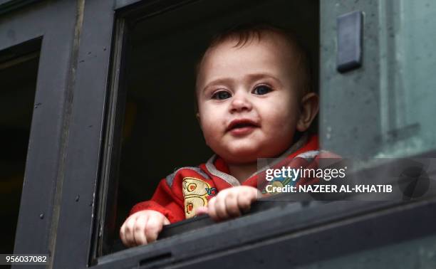 Syrian child, evacuated from a rebel-held area in Syria's central Homs province, looks from the window of a bus after arriving in a convoy at Abu...