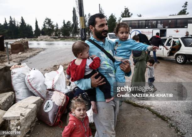 Syrian man walks carrying children upon arriving in a convoy at Abu al-Zandin checkpoint near al-Bab in northern Syria on May 8 after being evacuated...