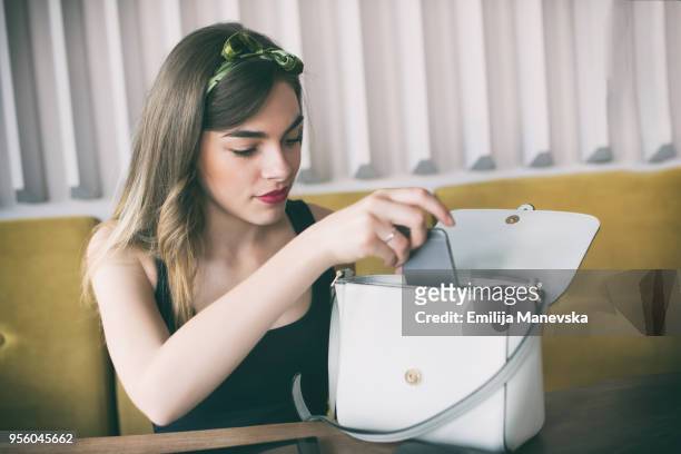 young beautiful woman sitting in restaurant and checking her purse - sac à main blanc photos et images de collection