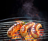 Grilled sausages on grill with smoke and flame