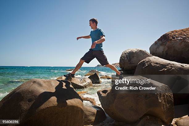 a man hops along boulders on the beach in the baths national park, virgin gorda, british virgin isla - walking side view bildbanksfoton och bilder