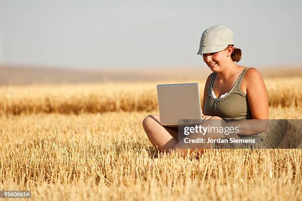 a young girl in a blue hat works on a laptop computer while sitting in the middle of a fresh cut gol - walla walla stockfoto's en -beelden