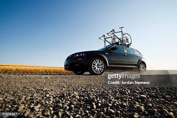 a black car with two road bikes on top cruises along a dirt road leaving a trail of dust in the dist - low angle view road stock pictures, royalty-free photos & images