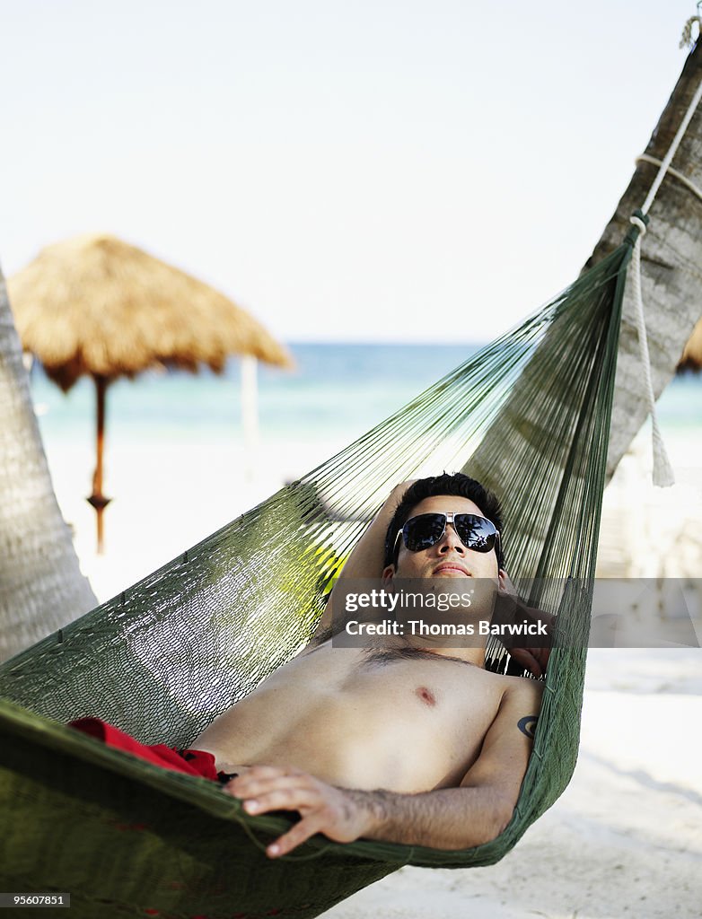Man lying in hammock on tropical beach