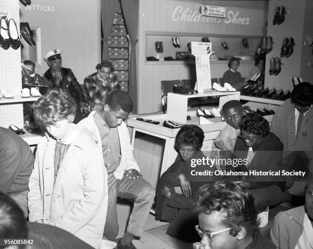 Photograph of young men and women and a policeman protesting segregation during a sit-in at John A Brown's Shoe Department, Oklahoma City, Oklahoma,...