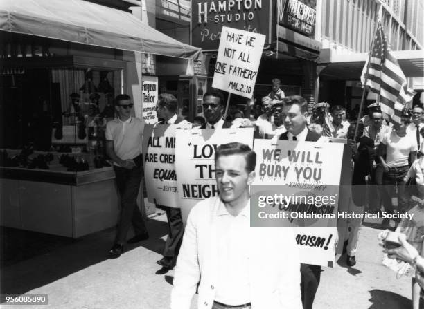 Photograph of Charlton Heston marching with a crowd of people protesting racism and segregation, Oklahoma City, Oklahoma, May 27, 1961. He is holding...