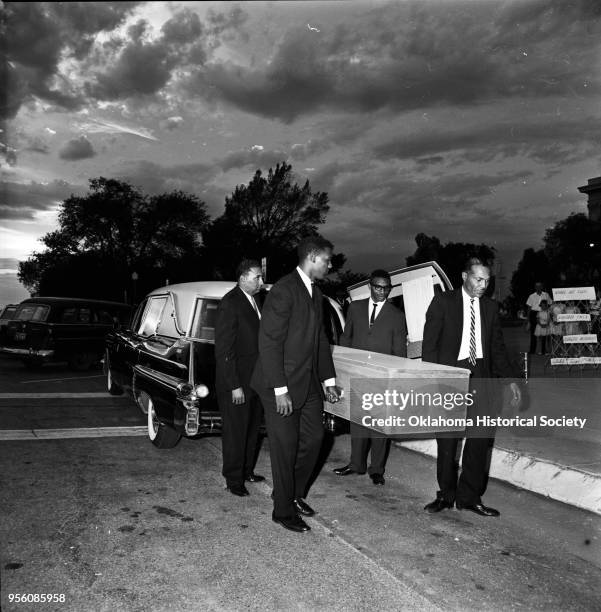 Photograph of Mr Sadbeer and Jethro Curry with two unidentified men who are moving a wooden casket from a hearse at a 'Jim Crow funeral' during an...
