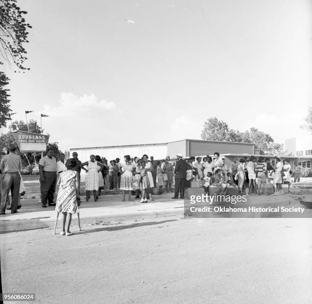 Photograph of a crowd of people at Douglass High School, Oklahoma City, Oklahoma, August 26, 1963. They are standing and seated with luggage, as they...