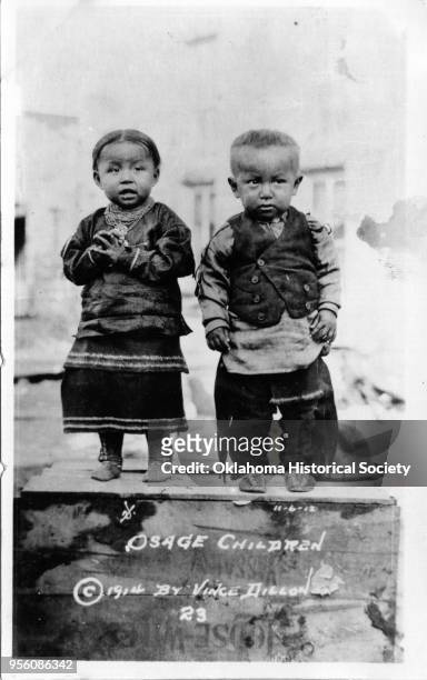 Photograph of Osage children Helen Grayhorse and John Blackbird Jr standing on a wooden box, November 6, 1912.
