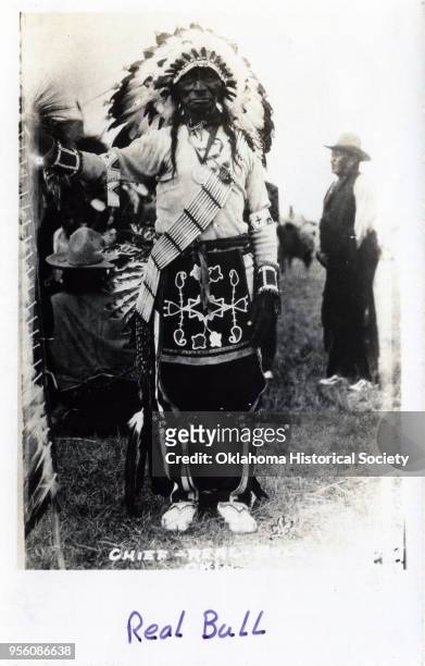 Photograph of Osage Chief Real Bull who is wearing a feathered headdress, a sash made of bone, and wearing an embroidered breechcloth, early...