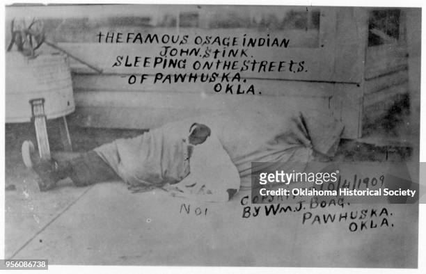 Photograph of 'the famous' Osage John Stink sleeping on the streets, Pawhuska, Oklahoma, October 4, 1909. A dog sits next to him.