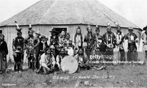 Photograph of a group of Osage male dancers posed around a large drum in front of the Gray Horse Hall roundhouse, Gray Horse, Oklahoma, circa 1913...