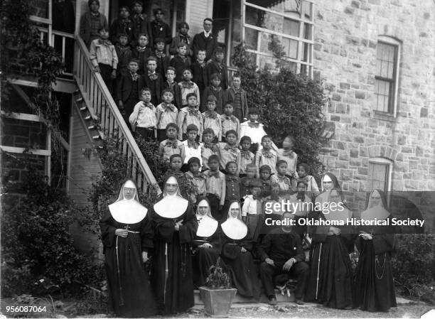 Photograph of Sisters of St Francis posing with Osage students at St John's Mission, Gray Horse, Osage Nation, Indian Territory, 1901. They are...