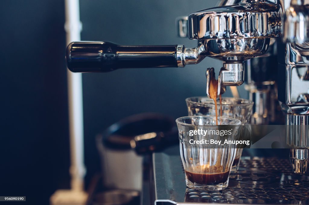 Cropped shot view of espresso pouring from coffee machine. Professional coffee brewing.